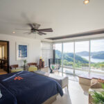 Primary suite with dark bedding and panoramic ocean views