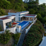 Exterior of the modern multi-level villa with its pool by day