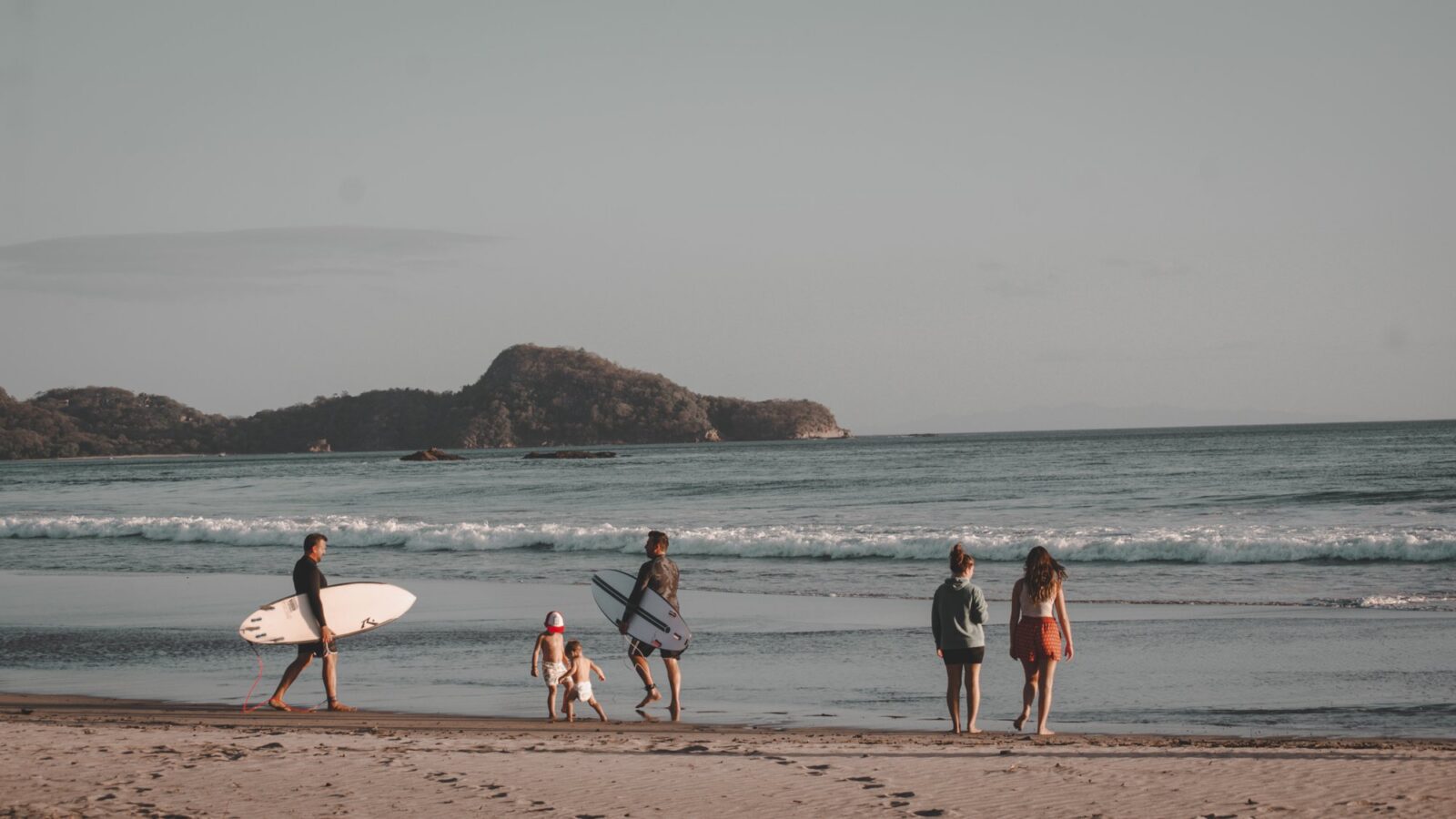 A family and surfers walking on the beach at sunset near San Juan del Sur, Nicaragua